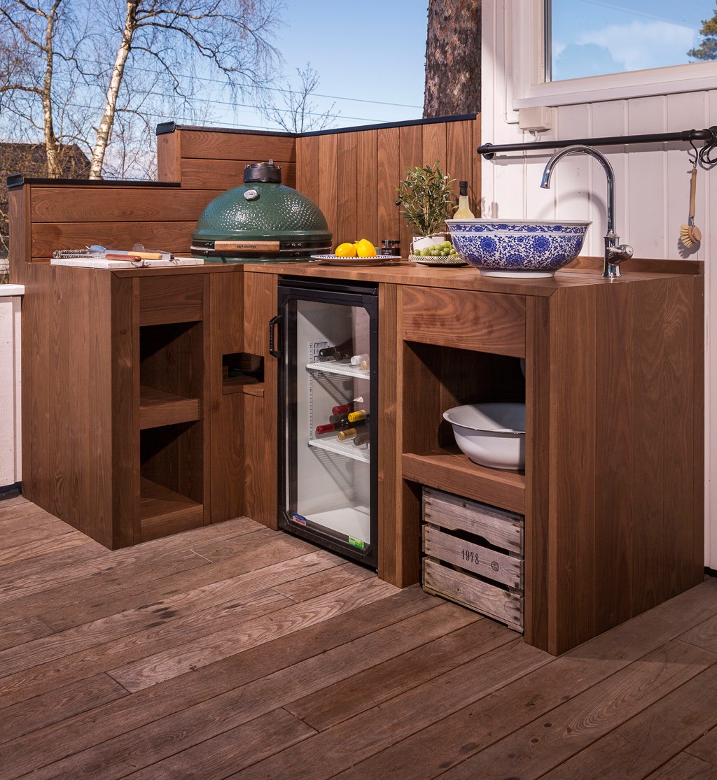 Utekjøkken i mørkt tre med grønn keramisk grill, innebygd vinskap, blå blomstrete vaskeskål