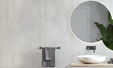 Moderne bad: betongvegg, rundt speil, sort armatur, hvit vask på lyst trebord og grå håndklær