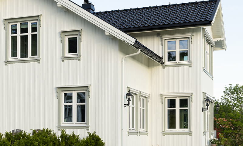 Hvit toetasjes trevilla med svart tak, hvite vinduer, utelamper og grønn hekk.