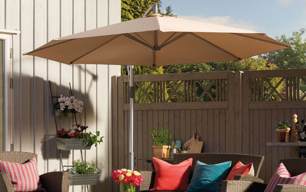 Inngjerdet terrasse med beige parasoll, rottingmøbler, fargerike puter og blomsterpotter.