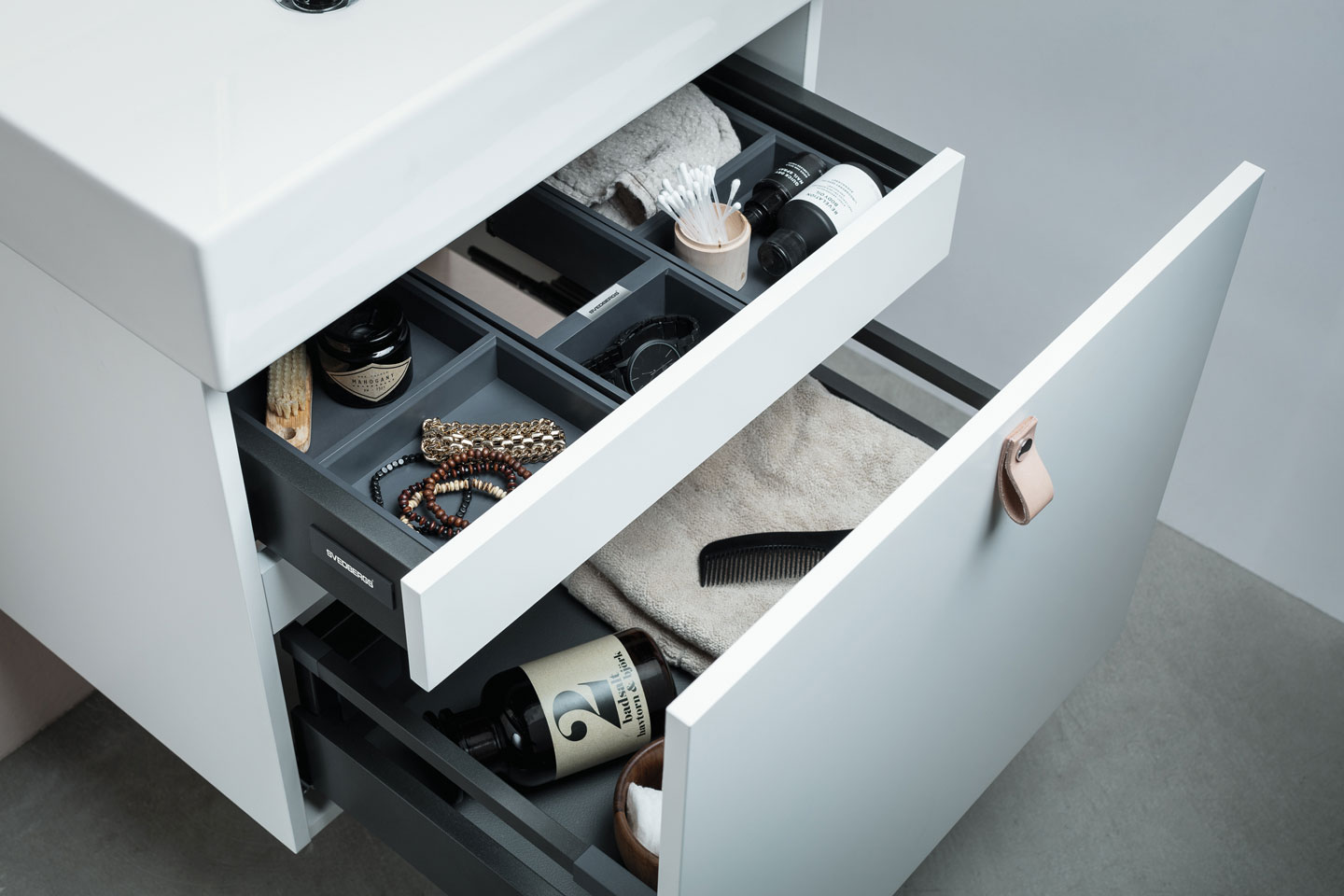 Åpne hvite baderomsskuffer med grå innsatser, smykker, håndkle, bomullspinner og såpeflaske