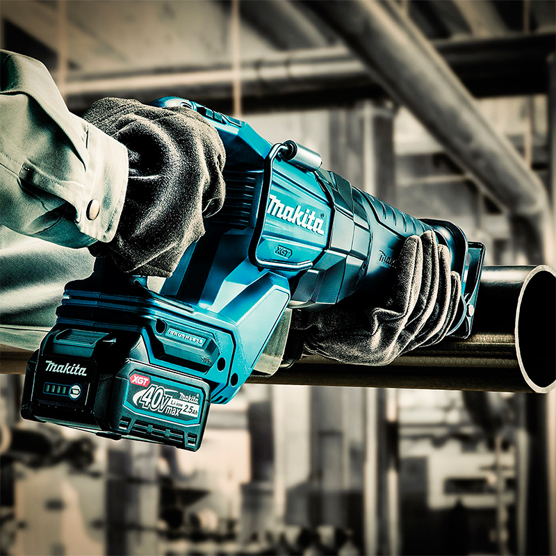 Hanskekledde hender holder blå Makita 40V XGT bajonettsag som kutter metallrør på byggeplass.