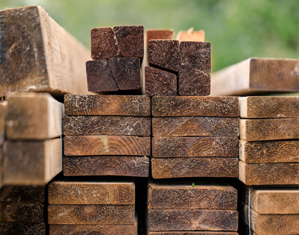 Stablet trelast: brune planker og firkantede bjelker mot uskarp grønn bakgrunn