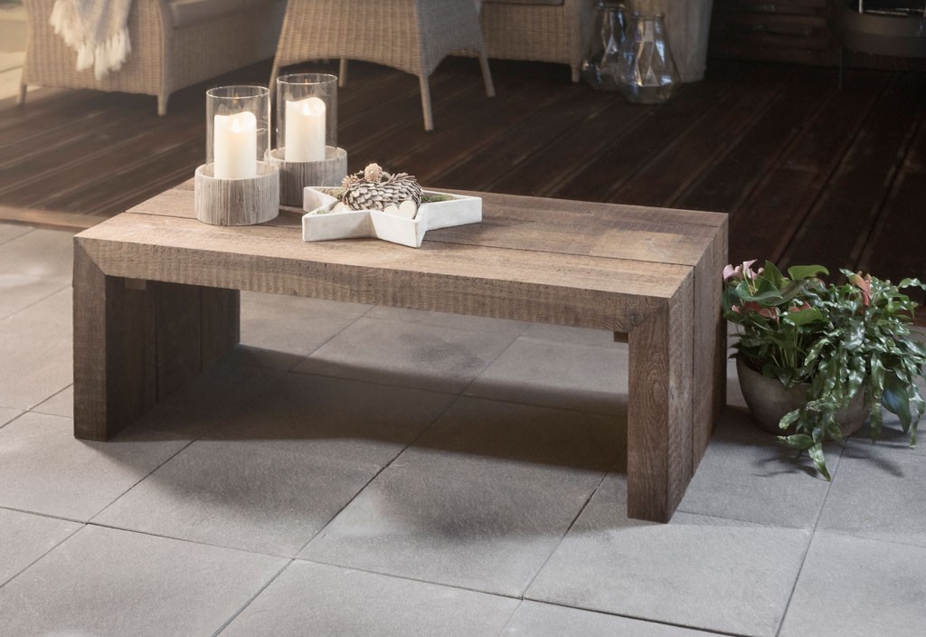 Rustikt, brunt trebord på grå fliser med to kubbelys, stjerneskål med kongler og grønn plante.