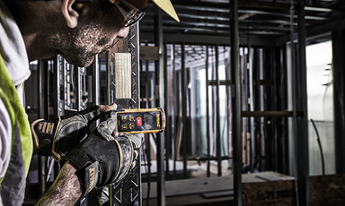 Bygningsarbeider i gul vest måler metallstendere med lasermåler i råbygg