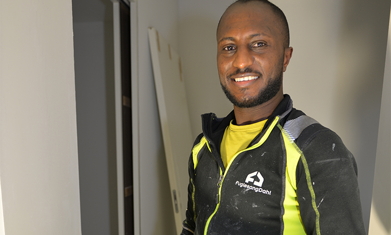 Byggarbeider i gul/svart arbeidsjakke med FuglesangDahl-logo i et rom under oppussing.