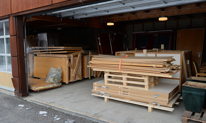 Åpen garasje med lysebrune treplater på paller, rustne stålbjelker og grått betonggulv