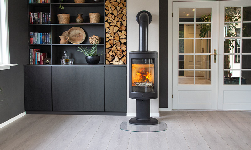 Moderne stue med svart vedovn med flammer, grått gulv, innebygd hylle med ved og dekor