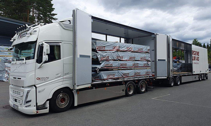 Hvit semitrailer med åpent sideplan og stabler plastinnpakkede trelastpakker fra Bergene Holm AS