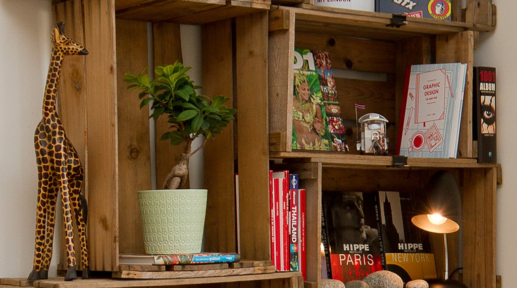 Stabel av rustikke trekasser med girafffigur, grønn potteplante, fargerike bøker og lampe