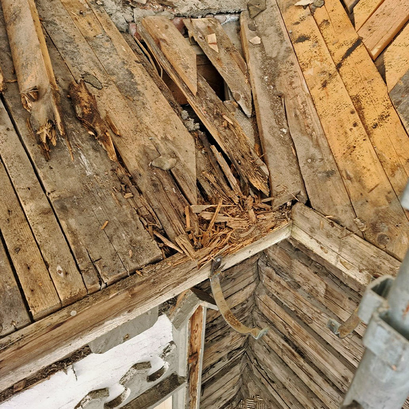 Slitt brunt tregulv med råtnende planker og en metallstropp i et loftshjørne