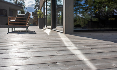 Lys treterrasse med moderne brun/beige stol, grønn potteplante og speilende glassdør.