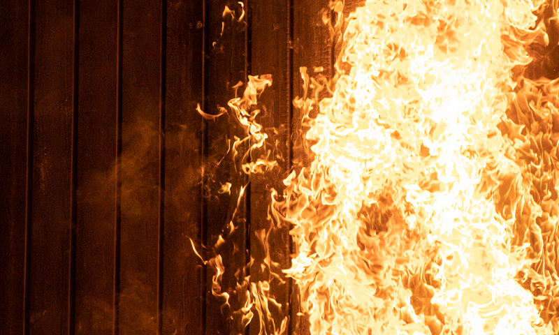 Kraftige oransje og gule flammer som sluker en mørk trevegg.