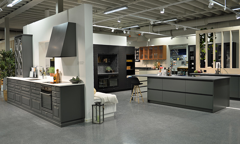 Moderne kjøkkenutstilling med mørkegrå skap, kjøkkenøy, hvite benkeplater og varme treflater