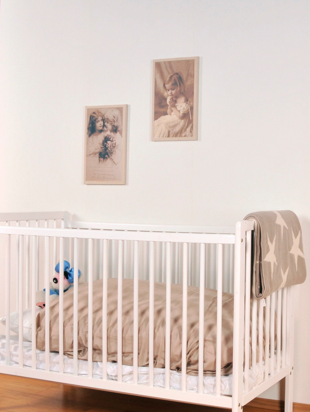 Hvit sprinkelseng med beige dyne, grått stjernepledd over siden og blå kosebamse under sepia bilder