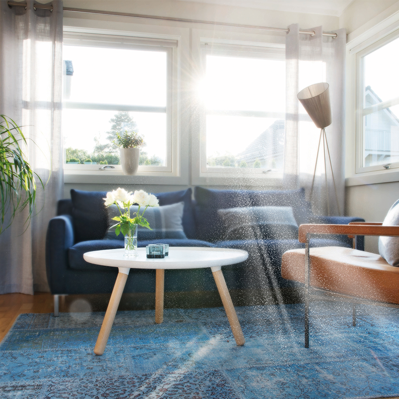 Lyst oppholdsrom med blå sofa, rundt hvitt bord med hvite roser, brun lenestol og store vinduer