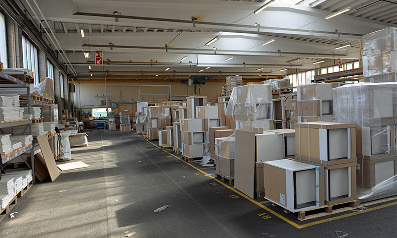 Lys lagerhall med stablede, innpakkede hvite og beige skap på paller.