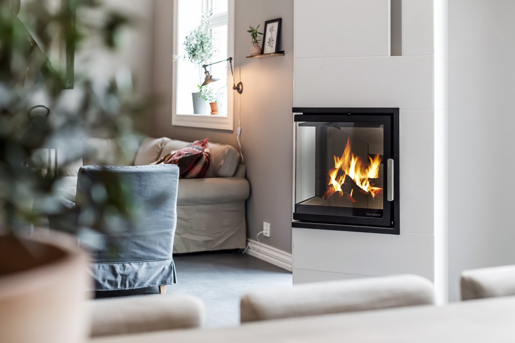 Moderne stue med grå sofa, peis med flammesyn gjennom svart ramme og vindu med planter.