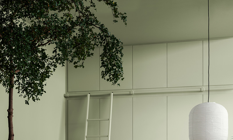 Minimalistisk rom med lysegrønne skap, hvit stige, hengende hvit papirlampe og trekvist.