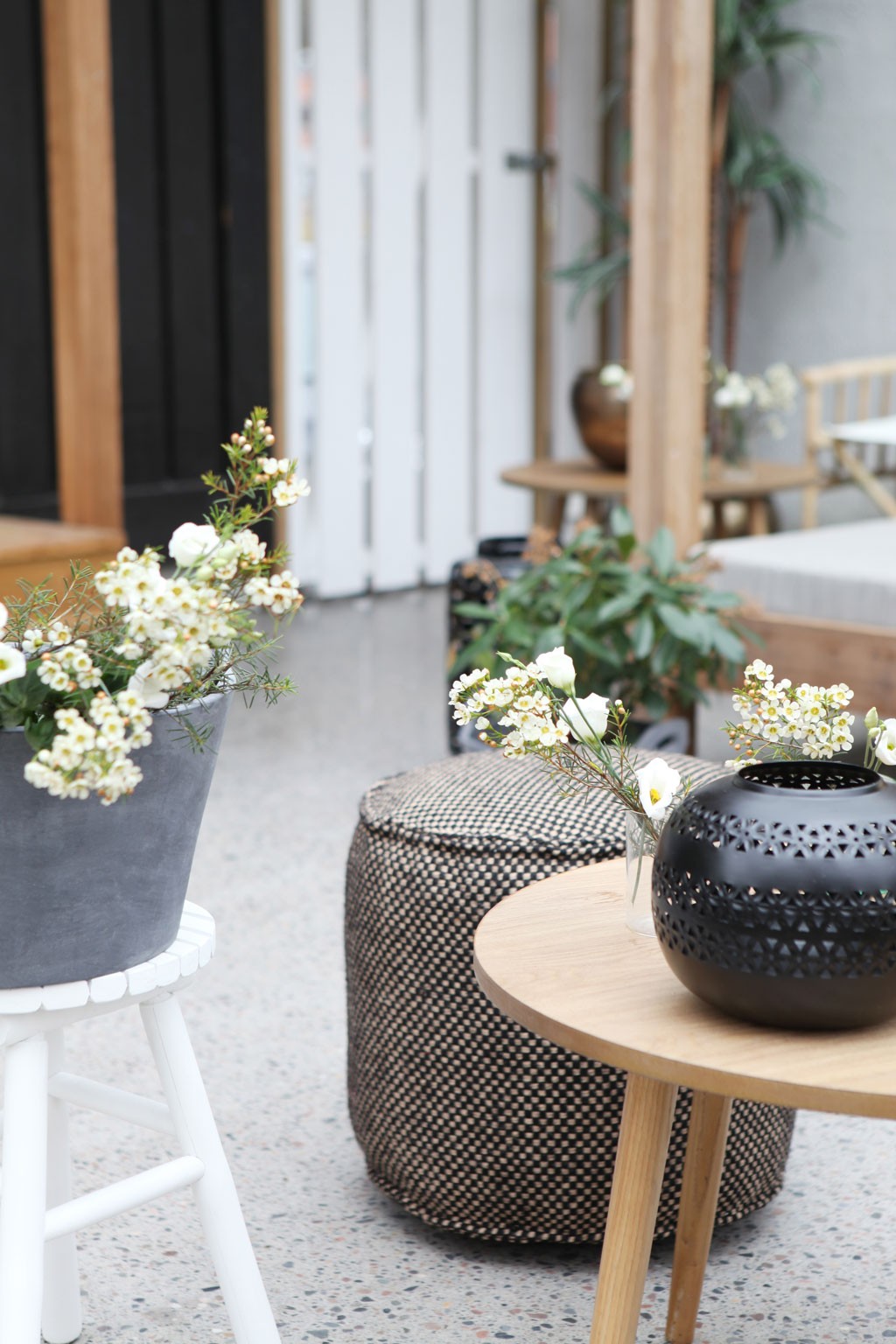 Uteplass med hvite blomster i grå potte og glassvase, svart dekorlykt og striet puff