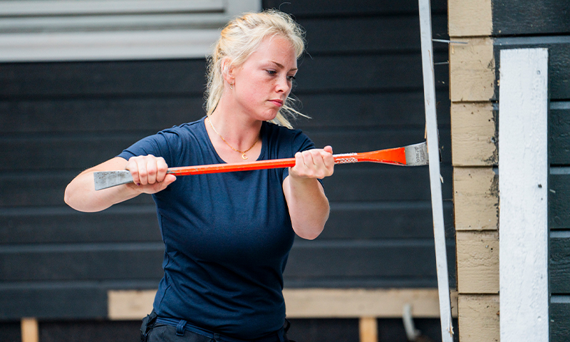 Kvinne i blå t-skjorte skraper svart husvegg med rød skrape.