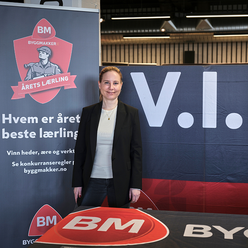 Person i svart jakke ved Byggmakker-stand i rødt og blått med logo og «Årets lærling»-tekst