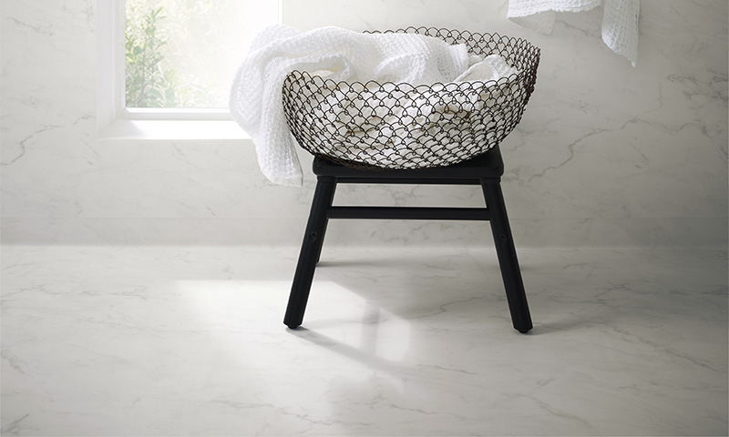 Svart metalltrådkurv med hvite håndklær på svart stativ ved solbelyst vindu i baderom.