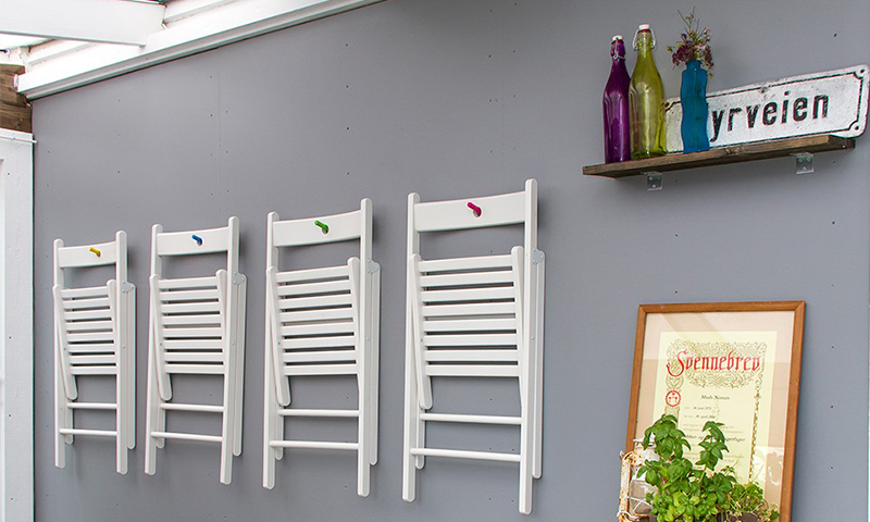 Fire hvite vegghengte stoler på grå vegg med fargekroker. Hylle med fargede flasker og ramme.