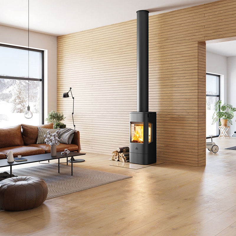 Lyst, moderne stue med svart vedovn, vedstabel, brun skinnsofa og store vinduer.