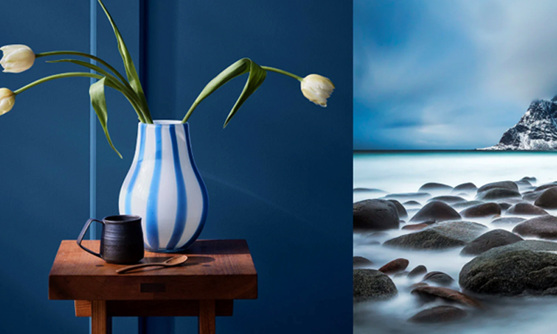 Delt: blå-hvit vase med gule tulipaner på trebord mot blå vegg, steinete kyst med disig sjø