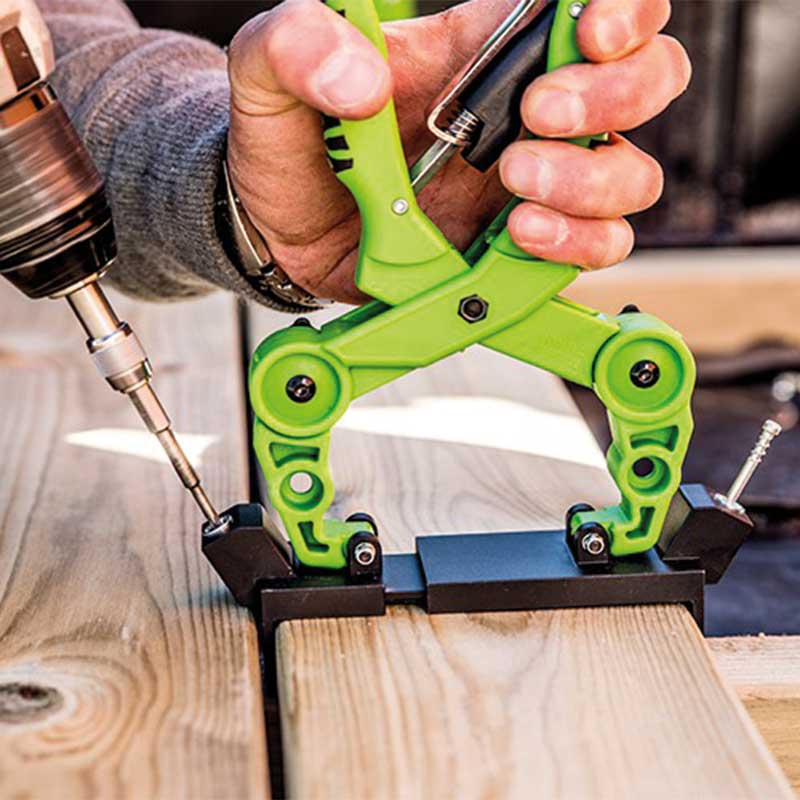 Hånd med grønn klemme holder to treplanker mens en drill skrur inn en skrue