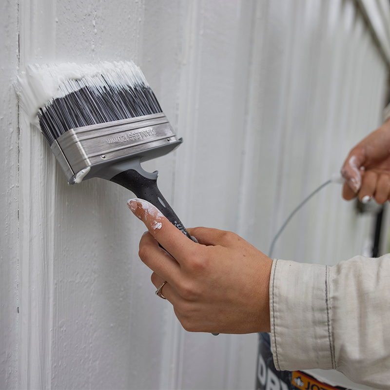 Nærbilde av hånd som maler hvit trepanel med bred pensel.