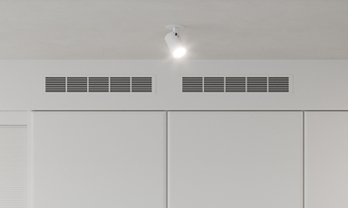 Hvit minimalistisk vegg med tre paneler, innebygde ventiler og ett takspot.