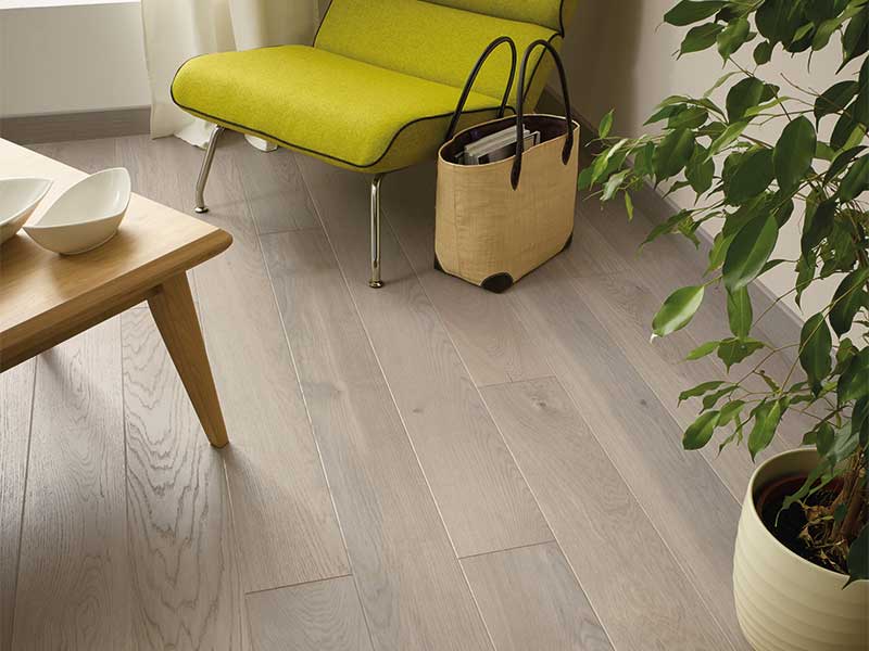 Hjørne med grønn lenestol på lyst tregulv, trebord med hvite skåler, beige stråveske og stor plante