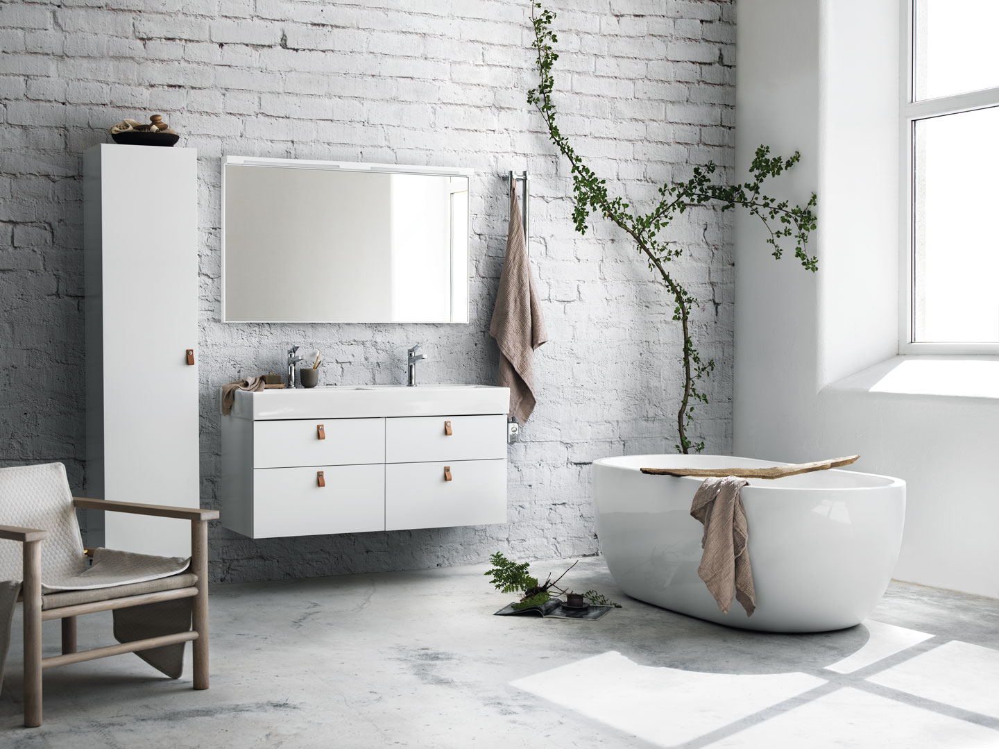 Lyst baderom med hvitt frittstående badekar, dobbel vask, grå murvegg og klatreplante.