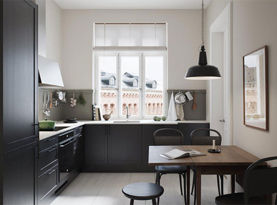 Lyst, moderne kjøkken med svarte skap, trebord, sort pendel og stort vindu mot murbygning.