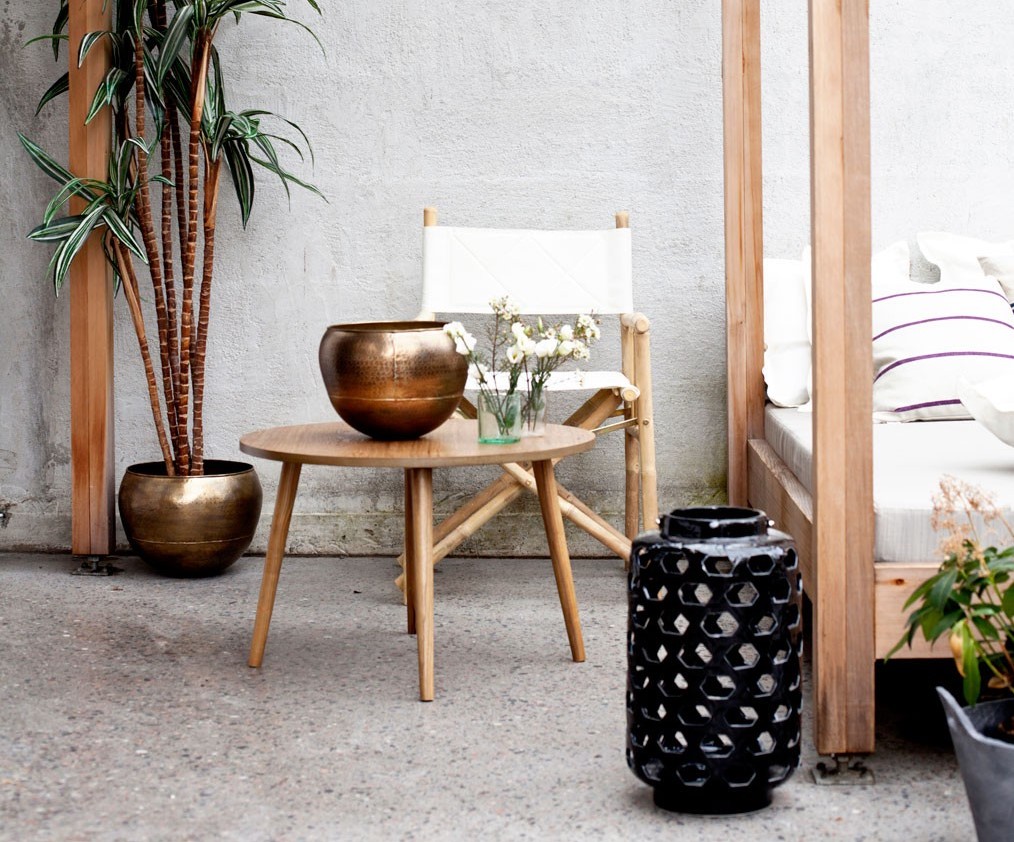 Utendørs lounge: lyst tre, hvit stol, bord med bronsefarget skål, planter og svart lykt