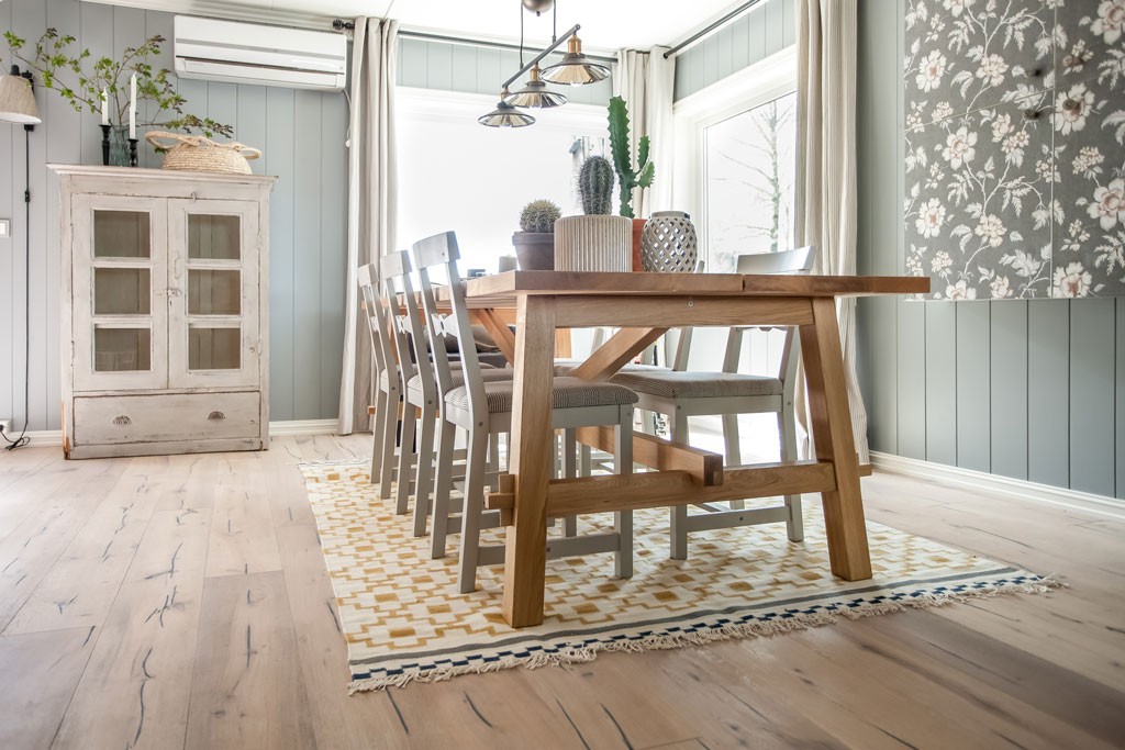 Lyst nordisk spiserom med trebord, seks grå stoler, mønstret gul-hvitt teppe og kaktus.