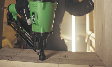 Nærbilde av grønn ESSVE-spikerpistol som fester spiker i treplate under byggearbeid.