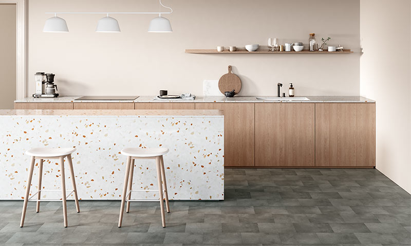 Moderne kjøkken i lyse beige- og tretoner med terrazzoøy, to hvite krakker og pendellamper.