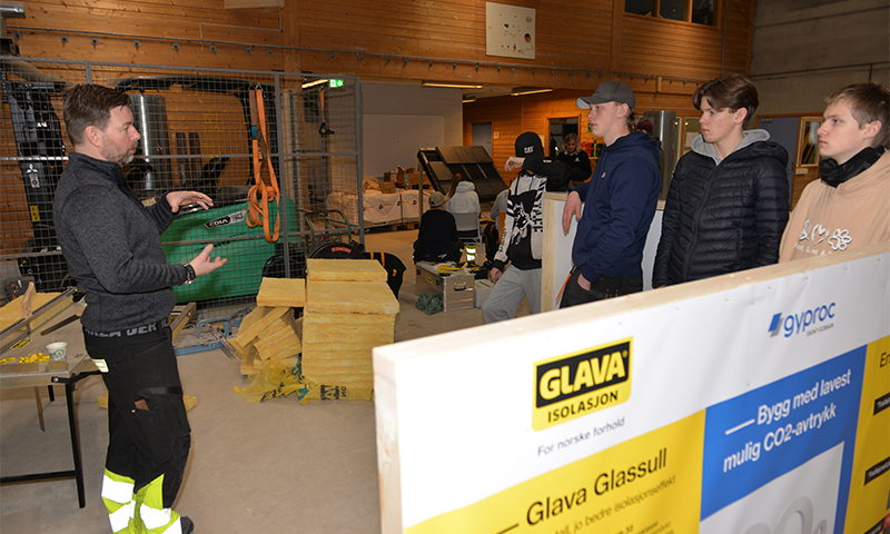 Arbeider viser gul glassull foran GLAVA-banner, flere tilskuere i verkstedhall.