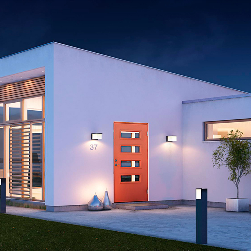 Hvit moderne husfasade om kvelden med oransje inngangsdør, vegglamper, potteplante og husnr. 37