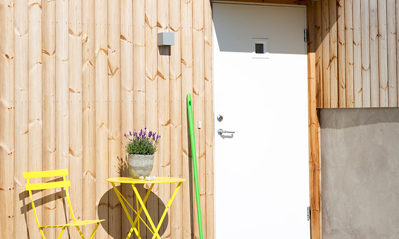 Lys trefasade med hvit inngangsdør, gul kafégruppe og lavendel i grå krukke