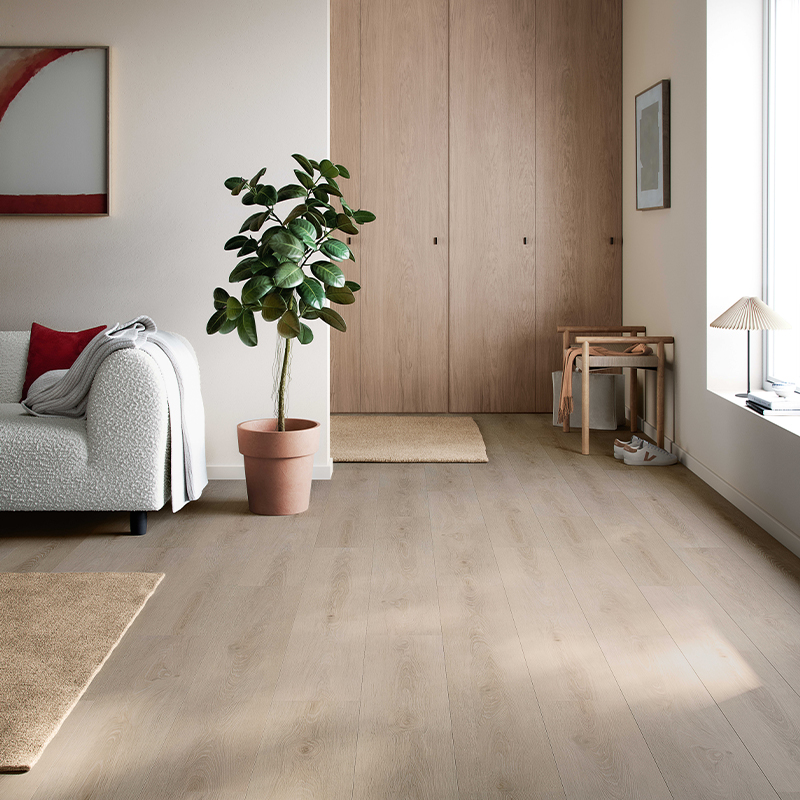 Lyst rom med lyse tregulv, hvit sofa med rødt putetrekk og grønn plante foran lyse tredører.