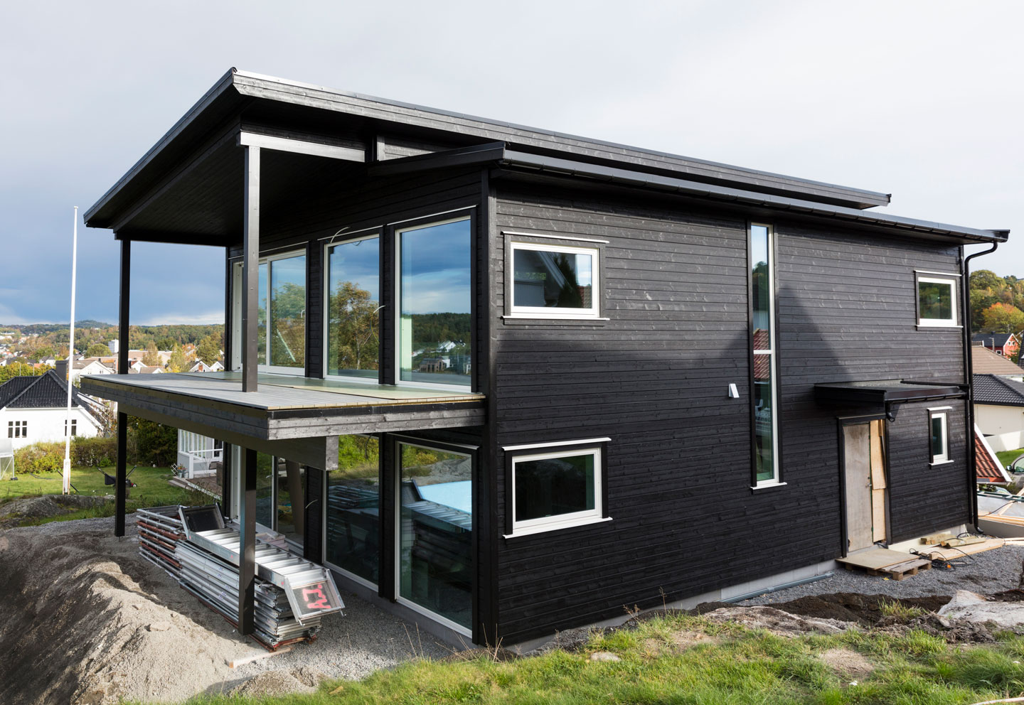 Moderne svart toetasjes hus med store vinduer, balkong og byggeutstyr i hagen
