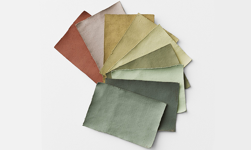 Vifte av tekstilprøver i jordfarger (rustrød, beige, gul, grønn) på hvit bakgrunn