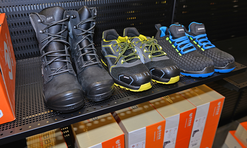 Tre par arbeidssko på butikkhylle: sorte støvler, svart-gule vernesko, svart-blå sko