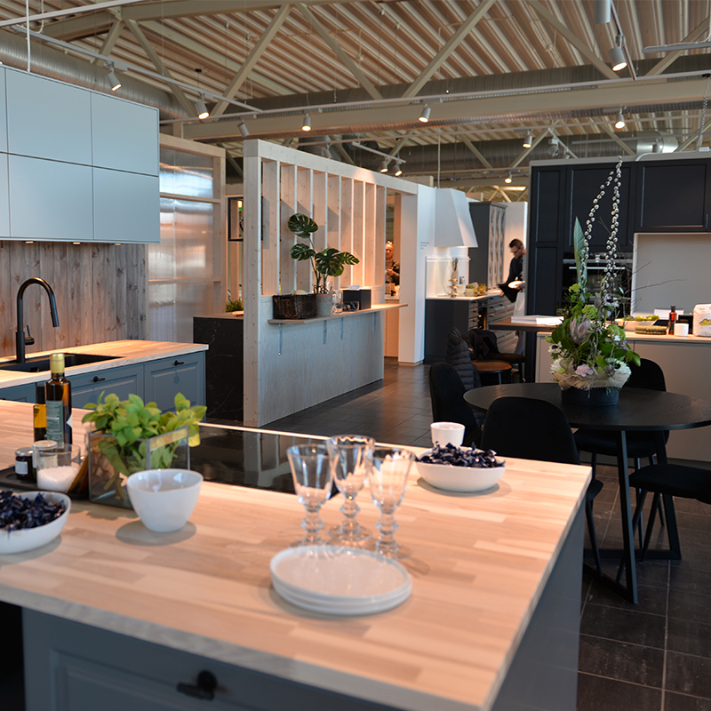 Moderne kjøkkenutstilling med lys trebordplate, gråblå skap, sorte stoler og blomster.