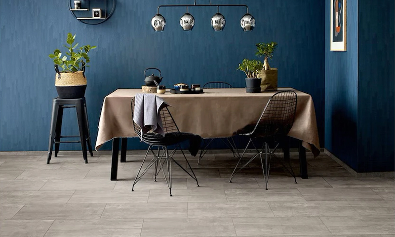 Spisestue med blå vegg, beige duk, svarte trådstoler, hengende speillamper og grønne planter.