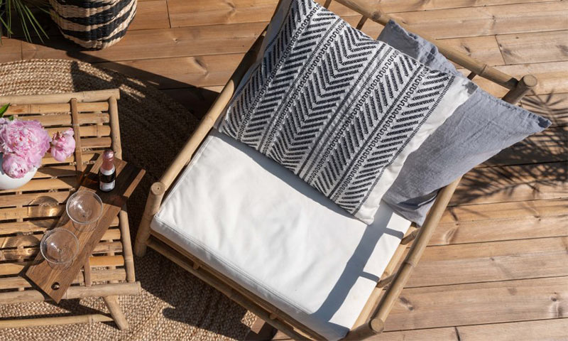 Solfylt terrasse med bambusstol, hvit pute, svart-hvitt mønsterpute, grå pute, rosa peoner og glass